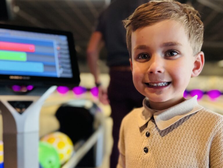 Jonge jongen lacht in bowlinghal met gekleurde bowlingballen en scorebord op achtergrond